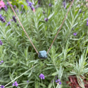 May include: A delicate gold chain necklace with a single, dark green, rough-cut gemstone pendant.