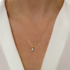 May include: A delicate gold chain necklace with a small oval opal pendant. The pendant is set in a gold pineapple design.