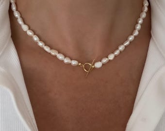 May include: A delicate pearl necklace with a gold toggle clasp. The necklace is made of small, white pearls and is perfect for adding a touch of elegance to any outfit.