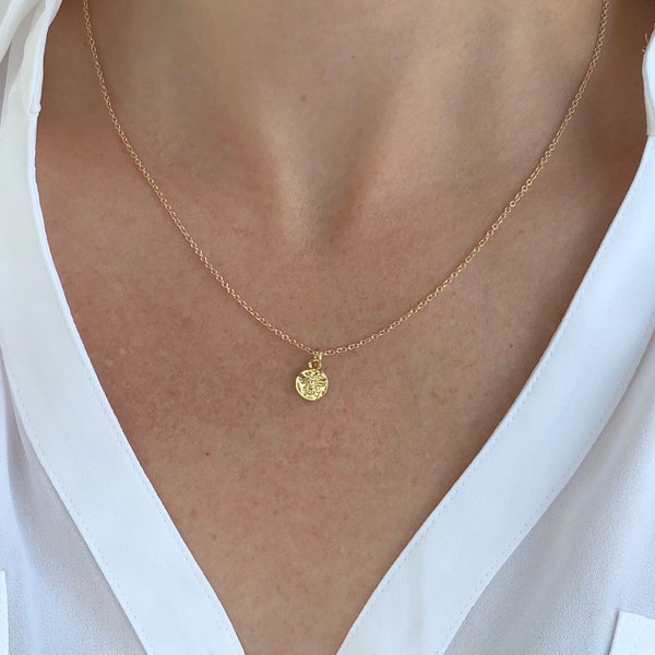 Könnte beinhalten: Eine zarte goldene Kettenkette mit einem kleinen, runden Anhänger. Der Anhänger hat eine strukturierte Oberfläche und scheint aus Gold zu sein.