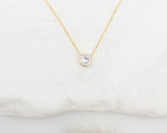 May include: A delicate gold chain necklace with a small round pendant featuring a clear crystal surrounded by smaller crystals.