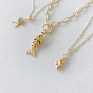 May include: Three gold-colored necklaces with ocean-themed pendants. One necklace features a starfish pendant, another has a fish pendant, and the third has a seahorse pendant. The chains vary in style, with one having a link chain.