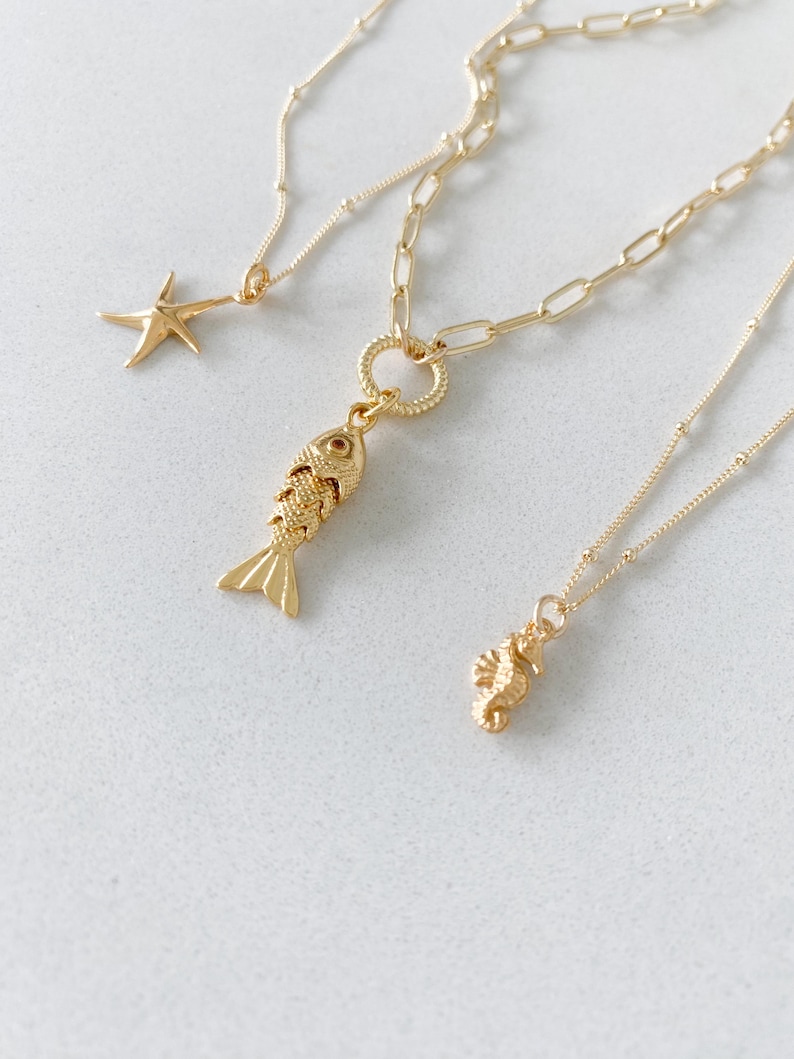May include: Three gold-colored necklaces with ocean-themed pendants. One necklace features a starfish pendant, another has a fish pendant, and the third has a seahorse pendant. The chains vary in style, with one having a link chain.