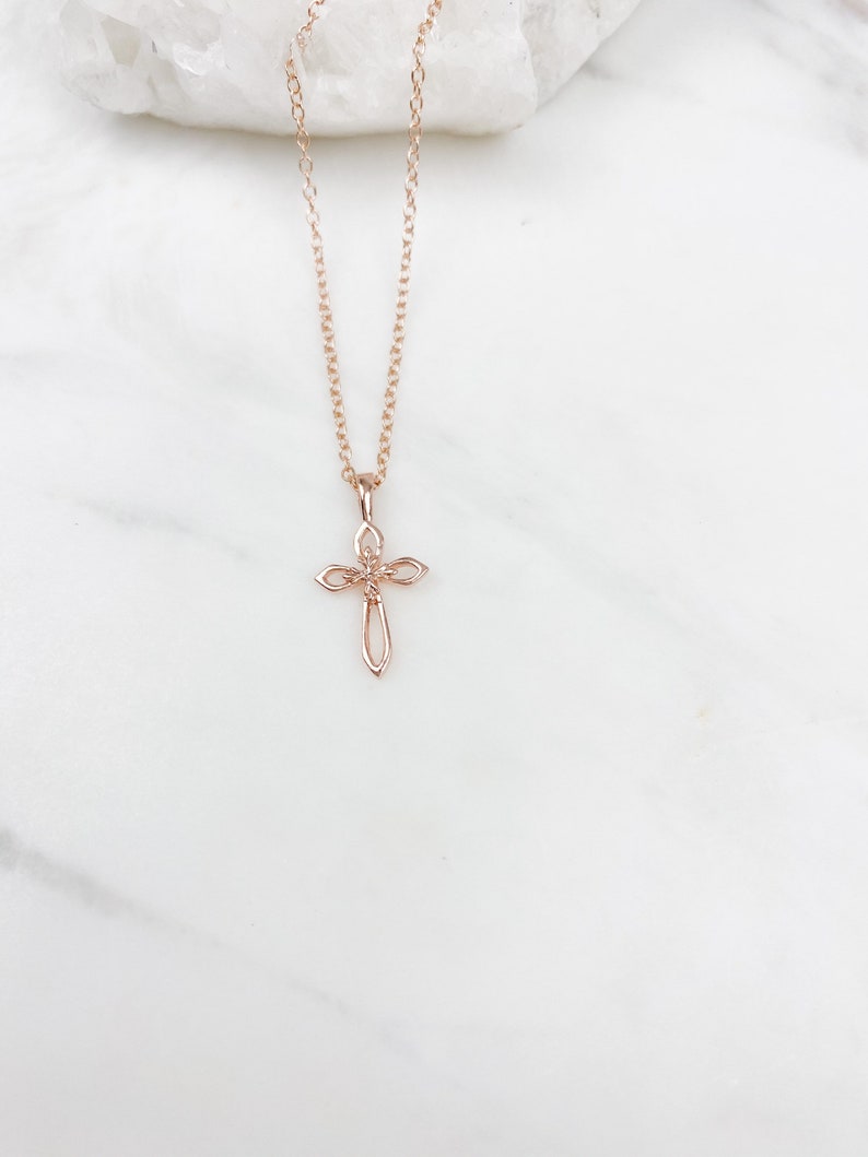Puede incluir: Un delicado collar de cadena de oro rosa con un peque&ntilde;o colgante de cruz adornado.