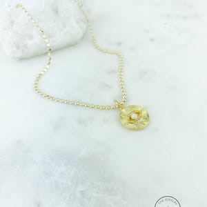 May include: Gold-toned necklace with a pendant featuring an eye design. The pendant is adorned with small, clear gemstones and a central pearl-like bead. The necklace is displayed on a white marble surface.