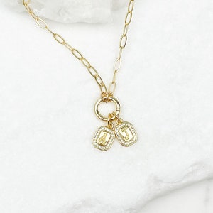 May include: A gold chain necklace with a circle charm and two rectangular charms with the letters "A" and "J" on them. The charms are set with small clear stones.
