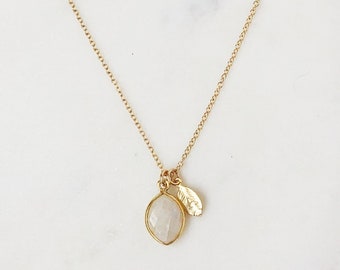 May include: A gold chain necklace with a white moonstone pendant and a small gold leaf charm.