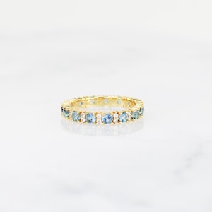 May include: A gold band ring with a row of blue gemstones and smaller clear gemstones.