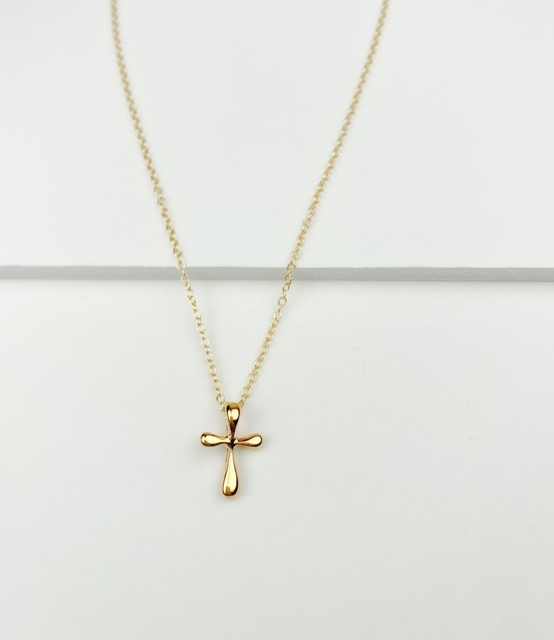 May include: A gold chain necklace with a small, simple gold cross pendant.