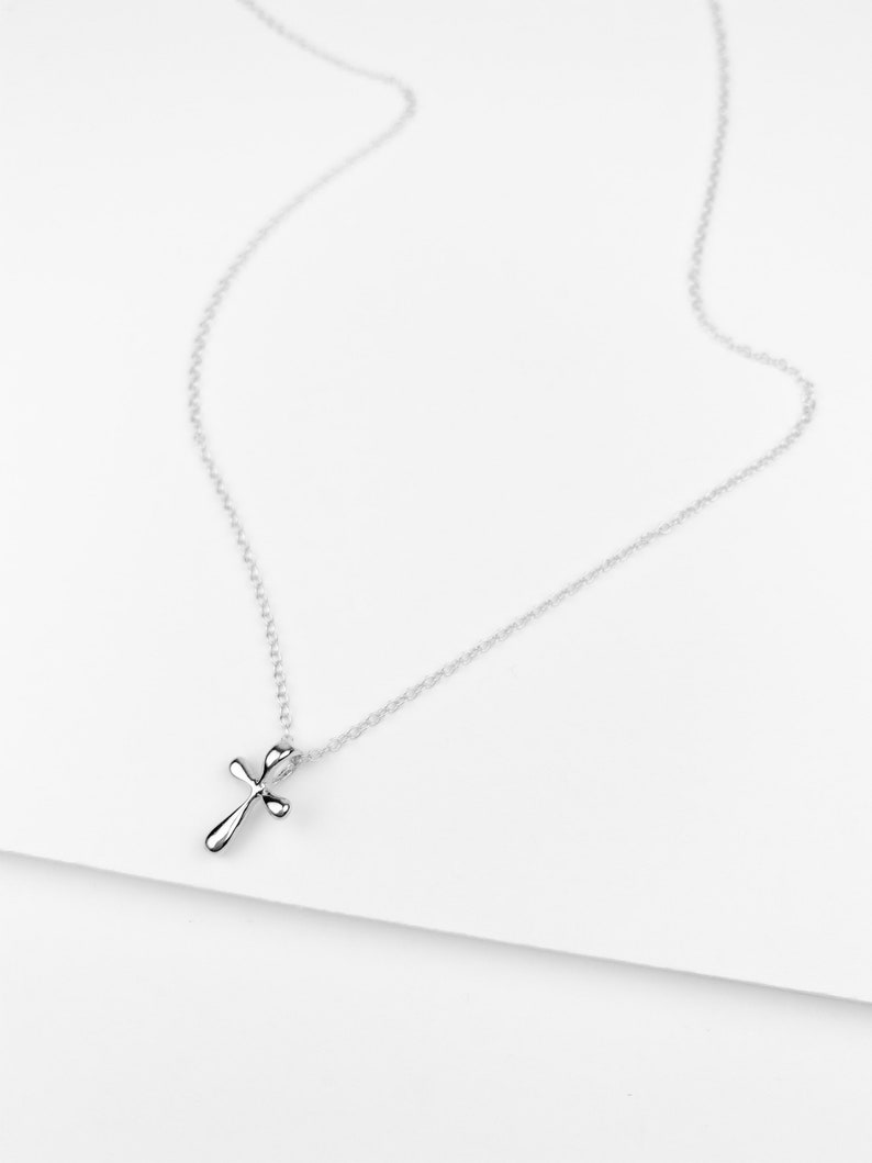 May include: A silver chain necklace with a small, simple silver cross pendant.