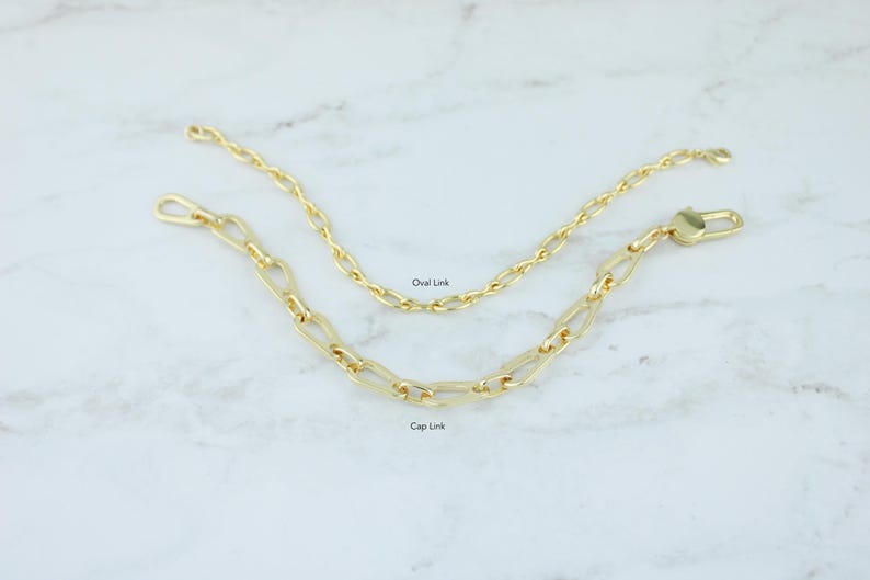 May include: Two gold-colored chain links, one with oval links and the other with cap links, are displayed on a white marble surface. The oval link chain is above the cap link chain. The text "Oval Link" and "Cap Link" are visible.