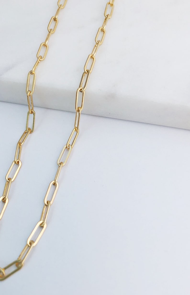 May include: A gold chain necklace with a delicate, linked design. The chain is made of small, oval-shaped links.