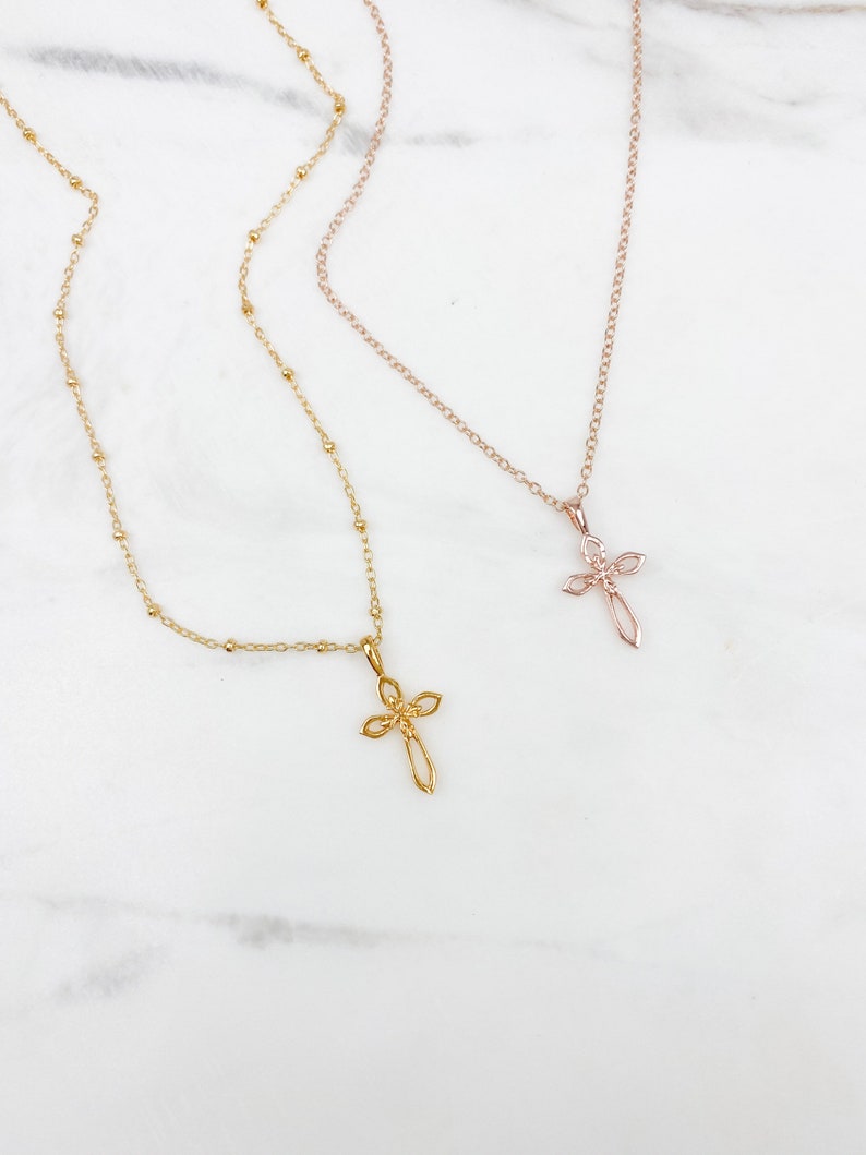 Puede incluir: Dos collares de oro con delicados colgantes de cruz. Uno es una cadena de oro rosa con un colgante de cruz m&aacute;s peque&ntilde;o, mientras que el otro es una cadena de oro con un colgante de cruz m&aacute;s grande.