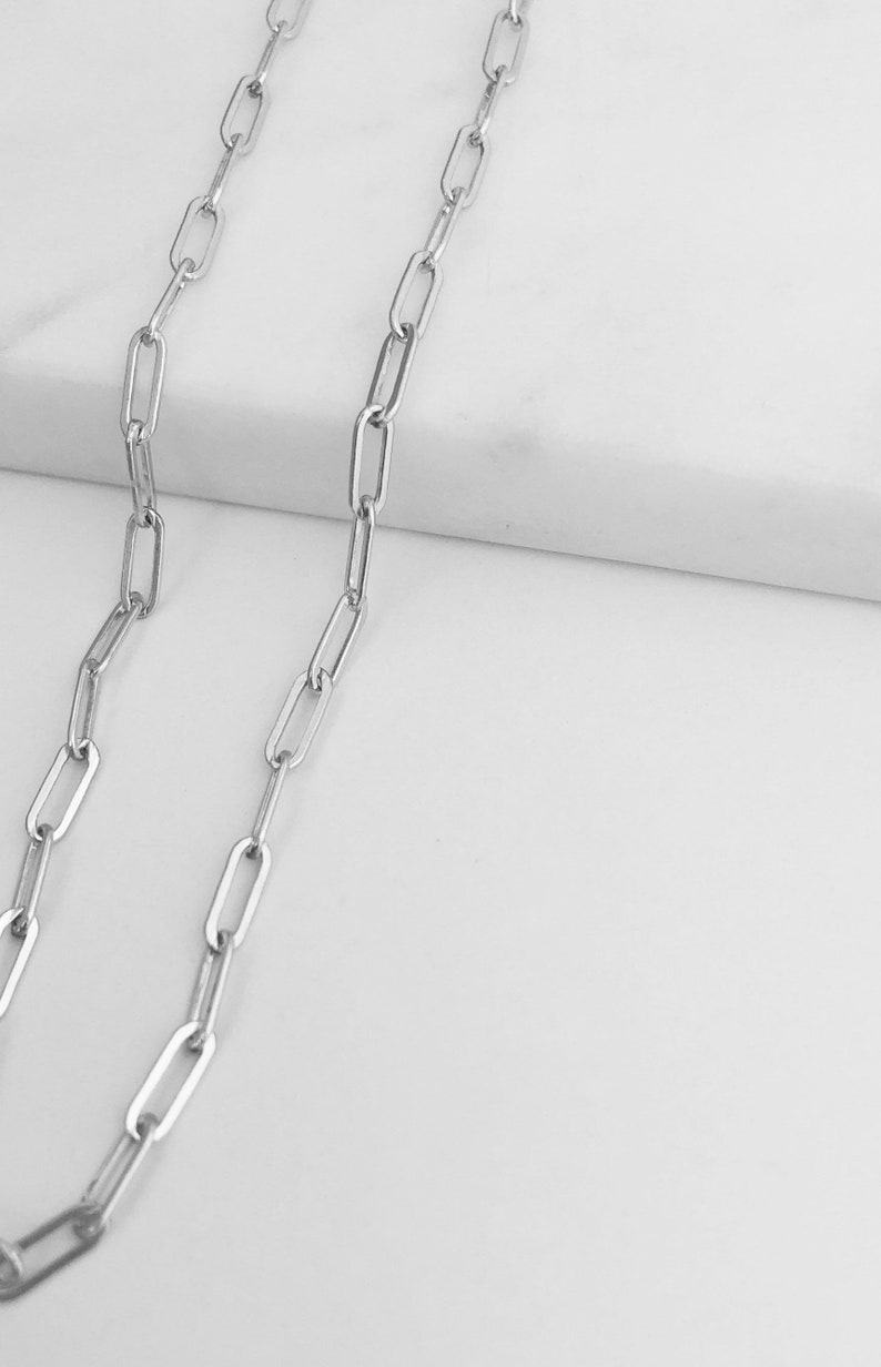 May include: A silver chain necklace with a simple, linked design. The chain is made of small, rectangular links.
