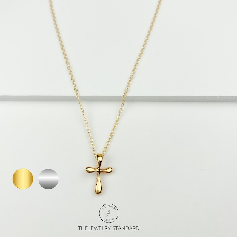 May include: A gold chain necklace with a small, gold cross pendant. The chain is delicate and the cross is simple in design. The necklace is displayed on a white background.
