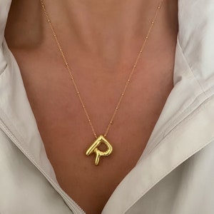 May include: A gold chain necklace with a chunky, abstract letter 'P' pendant.