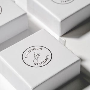 Peut inclure: Bo&icirc;tes carr&eacute;es blanches avec un logo circulaire noir qui indique "The Jewelry Standard" avec une lettre stylis&eacute;e "J" &agrave; l'int&eacute;rieur du cercle.