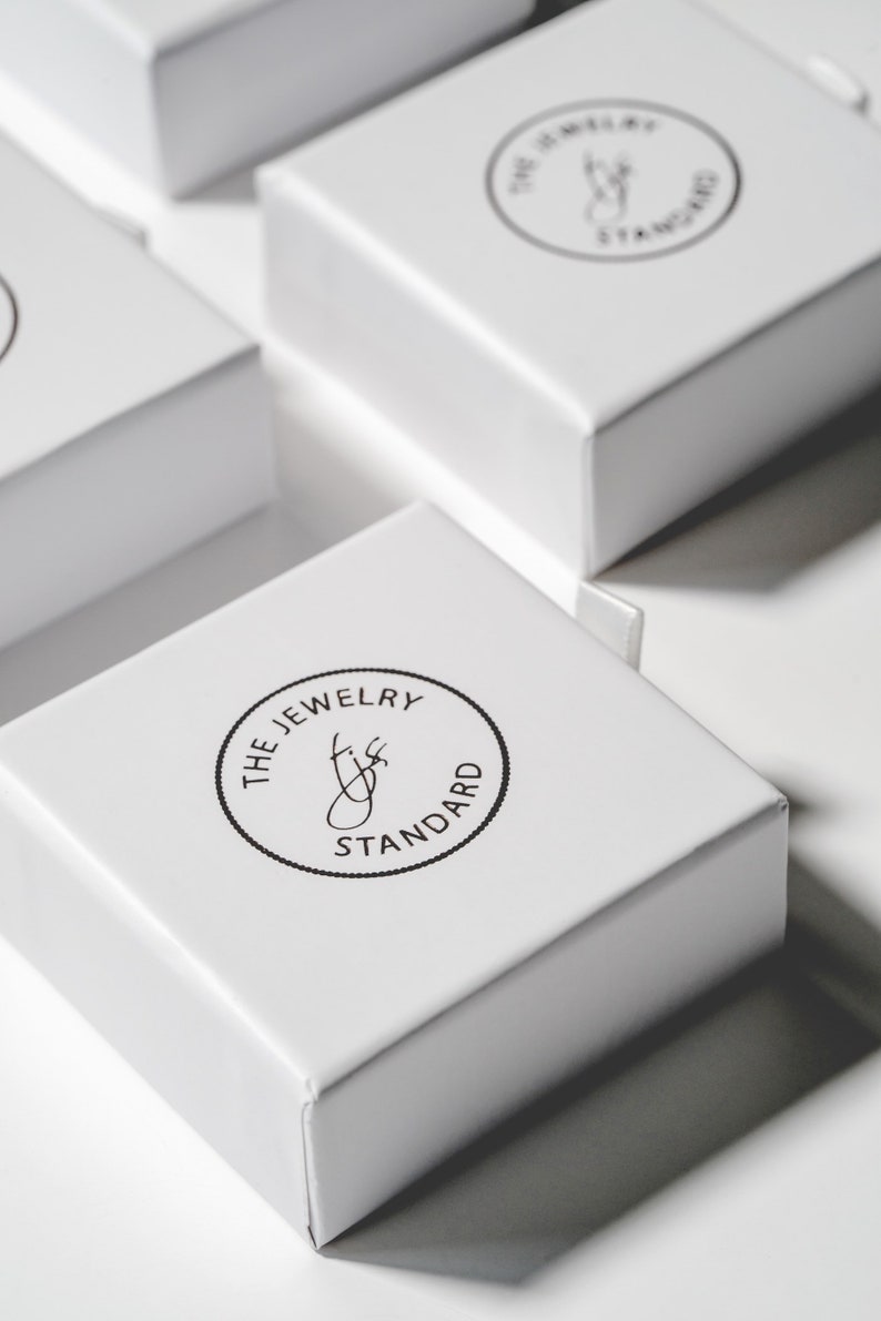 Peut inclure: Bo&icirc;tes carr&eacute;es blanches avec un logo circulaire noir qui indique "The Jewelry Standard" avec une lettre stylis&eacute;e "J" &agrave; l'int&eacute;rieur du cercle.