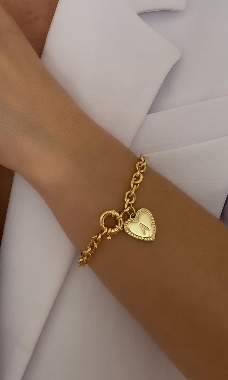 May include: A gold chain bracelet with a heart-shaped charm. The charm has a raised letter "A" on it.