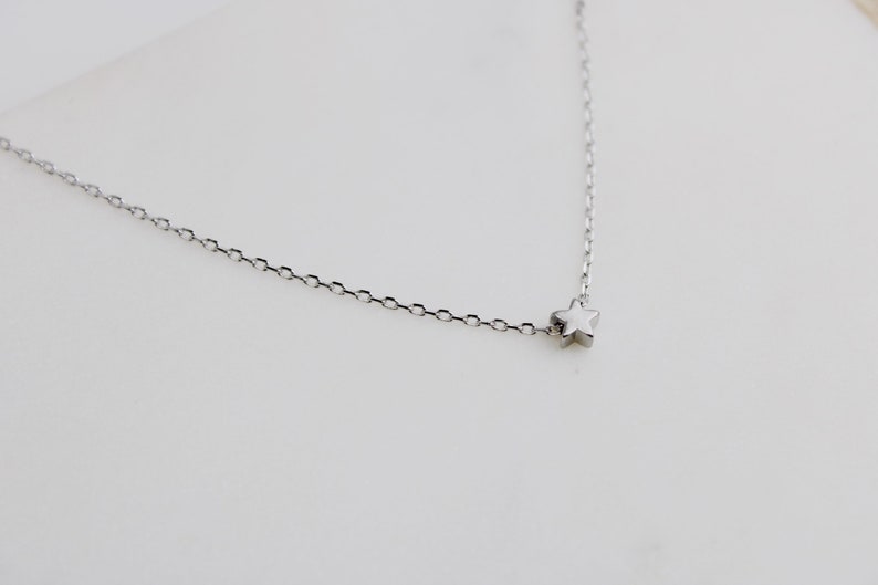 Peut inclure: Un collier fin en argent avec un petit pendentif en forme d'&eacute;toile.