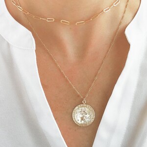 May include: A gold chain necklace with a large, round pendant featuring a detailed design. The pendant is a religious medallion with a raised image of a person.