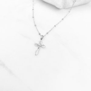 Puede incluir: Un collar de cadena de plata con un delicado colgante de cruz de plata. La cruz tiene un dise&ntilde;o simple y elegante con una peque&ntilde;a piedra transparente en el centro.