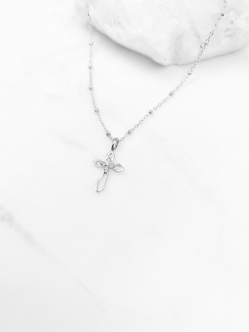 Puede incluir: Un collar de cadena de plata con un delicado colgante de cruz de plata. La cruz tiene un dise&ntilde;o simple y elegante con una peque&ntilde;a piedra transparente en el centro.