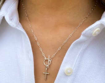 May include: A silver chain necklace with a toggle clasp and a small silver cross pendant.