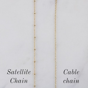 K&ouml;nnte beinhalten: Zwei goldene Ketten, eine mit einem Satellitenketten-Design und die andere mit einem Kabelketten-Design. Die Ketten h&auml;ngen vor einem wei&szlig;en Hintergrund. Der Text "Satellite Chain" befindet sich unter der linken Kette und der Text "Cable Chain" unter der rechten Kette.