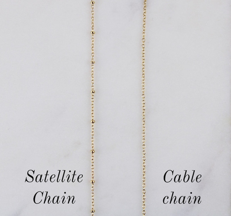 K&ouml;nnte beinhalten: Zwei goldene Ketten, eine mit einem Satellitenketten-Design und die andere mit einem Kabelketten-Design. Die Ketten h&auml;ngen vor einem wei&szlig;en Hintergrund. Der Text "Satellite Chain" befindet sich unter der linken Kette und der Text "Cable Chain" unter der rechten Kette.