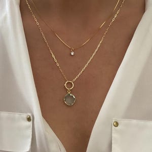 May include: A gold chain necklace with a small clear gemstone pendant and a larger clear gemstone pendant with a gold ring.