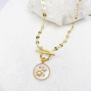 May include: Gold chain necklace with a toggle clasp and a white mother-of-pearl pendant featuring a sun, moon, and stars design.