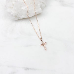 Puede incluir: Un delicado collar de oro rosa con un peque&ntilde;o colgante de cruz intrincado. La cadena es de estilo simple de eslabones finos.