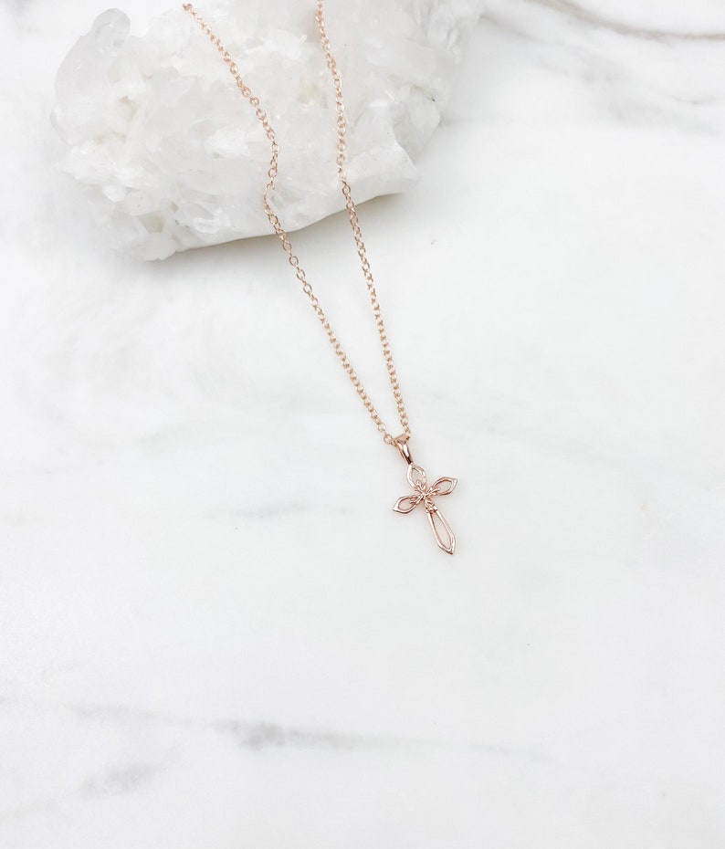 Puede incluir: Un delicado collar de oro rosa con un peque&ntilde;o colgante de cruz intrincado. La cadena es de estilo simple de eslabones finos.