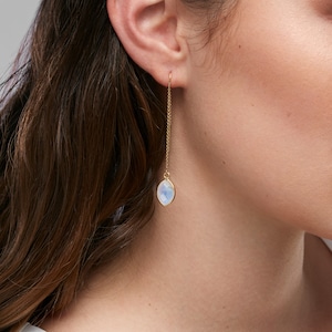 May include: Gold chain earrings with a white oval gemstone pendant.