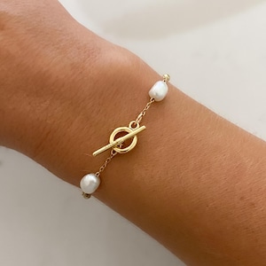 May include: A gold chain bracelet with a toggle clasp and white pearl accents.