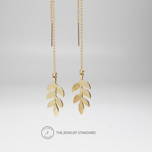May include: Gold leaf dangle earrings with a delicate chain and a small, textured leaf design. The earrings are suspended from a thin gold chain.