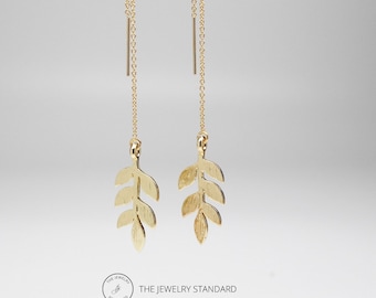 May include: Gold leaf dangle earrings with a delicate chain and a small, textured leaf design. The earrings are suspended from a thin gold chain.