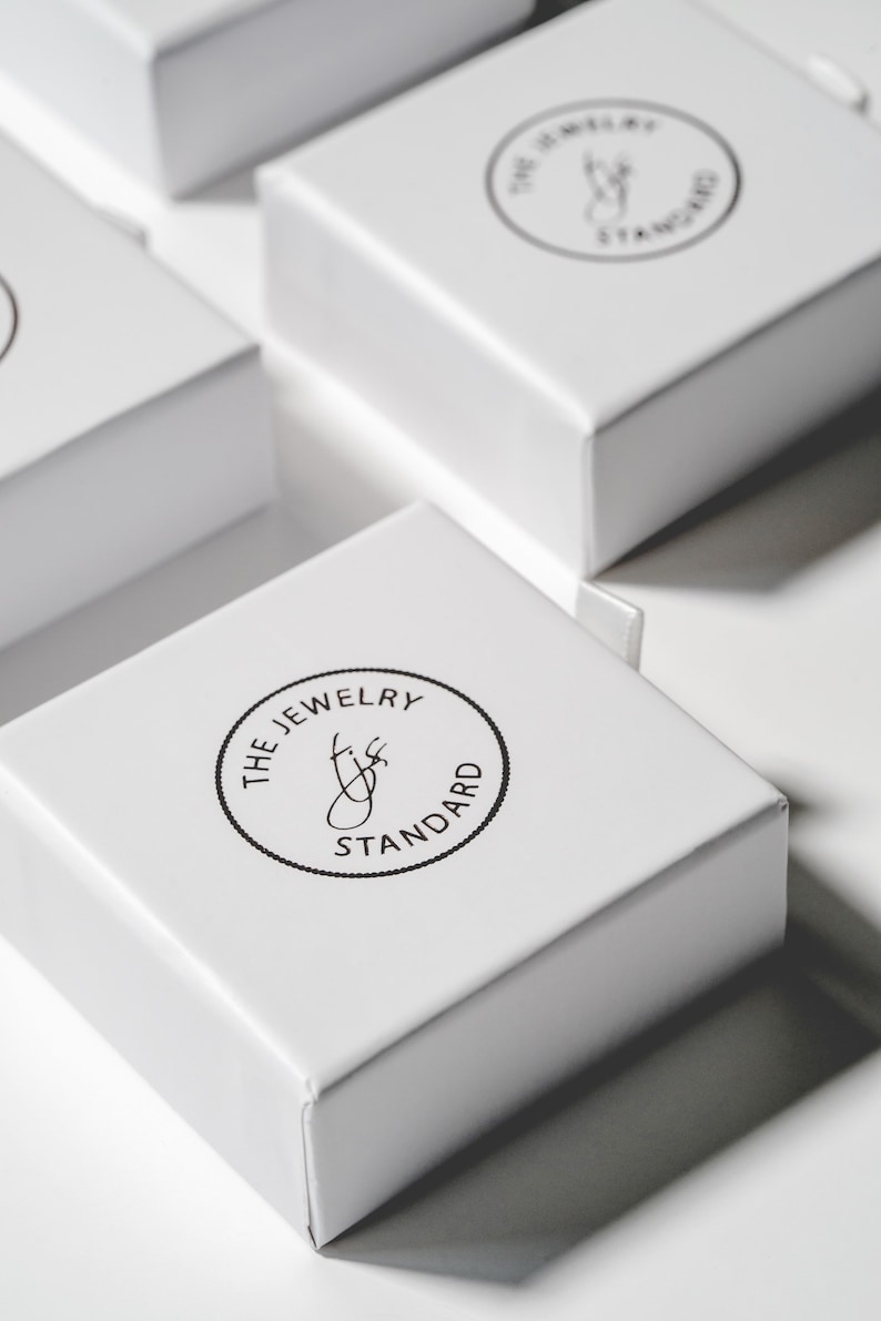 May include: Several white square boxes with the text "THE JEWELRY STANDARD" printed in a black circular design on the top. The boxes are arranged in a close-up shot, with some boxes partially visible.
