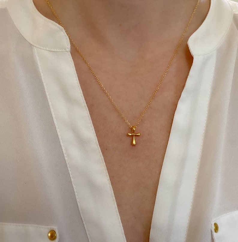 May include: A gold chain necklace with a small, simple gold cross pendant.