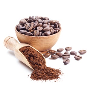 K&ouml;nnte beinhalten: Eine Holzschale gef&uuml;llt mit ger&ouml;steten Kaffeebohnen, daneben ein Holzsch&ouml;pfer, der Kaffeepulver ausgie&szlig;t. Mehrere ganze Bohnen sind verstreut. Das Bild ist vor einem wei&szlig;en Hintergrund, der die satten Braunt&ouml;ne des Kaffees hervorhebt.