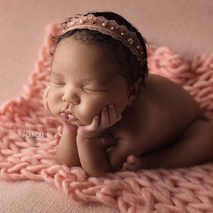 Può includere: Una neonata, una bambina, con un cerchietto rosa con strass, dorme su una coperta di maglia rosa.