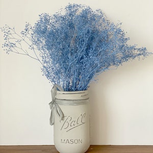 May include: A light blue bouquet of baby's breath flowers in a white painted Ball Mason jar with a gray ribbon.