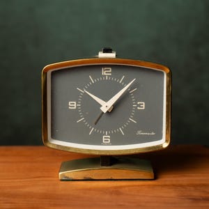 Peut inclure: Un réveil vintage de couleur or avec un cadran noir et des aiguilles blanches. L'horloge a une forme rectangulaire et un design simple. Le cadran de l'horloge a les chiffres 3, 6, 9 et 12 imprimés en blanc. Le cadran de l'horloge a également le mot "Temmarite" imprimé en blanc.