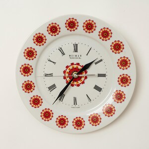 Peut inclure: Horloge murale en céramique blanche avec des aiguilles noires et des chiffres romains. Le cadran présente un motif floral central et une bordure d'accents floraux rouges et jaunes. L'horloge est marquée "WEIMAR" et "MADE IN JAPAN".