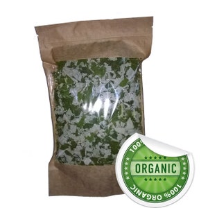 May include: A brown paper bag with a clear plastic window, containing a large amount of dried green leafy herbs. A white sticker with a green circle and the text "100% ORGANIC" is attached to the bag.