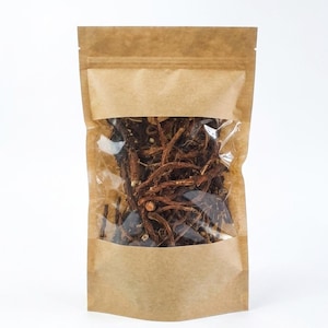 Peut inclure: Un sachet debout en papier kraft brun doté d'une fenêtre rectangulaire transparente sur le devant. Le sachet est rempli d'une collection de fines racines ligneuses ou de tiges herbacées séchées brun foncé visibles à travers la partie plastique.