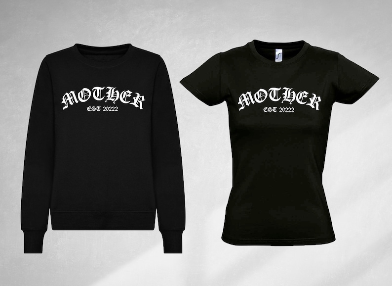 K&ouml;nnte beinhalten: Schwarzer Pullover und T-Shirt mit dem Text "MOTHER EST 2022" in wei&szlig;en gotischen Buchstaben.