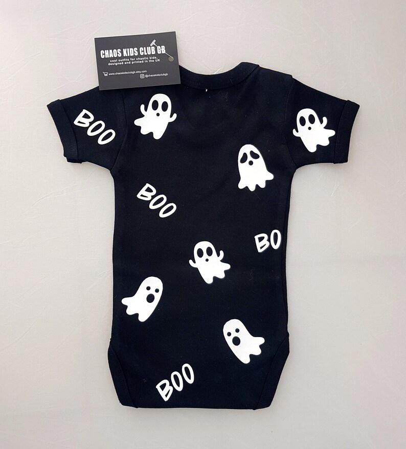 May include: Black baby onesie with white ghost and "BOO" designs. The onesie is made by Chaos Kids Club GB.