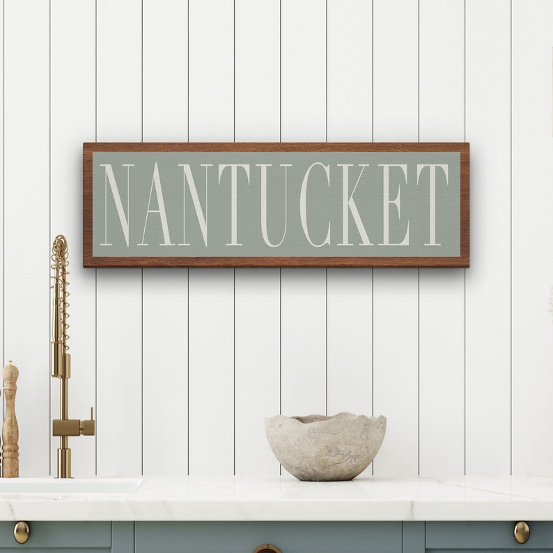 May include: A wooden sign with a light green background and the word "NANTUCKET" in white lettering. The sign is framed in a dark wood frame.